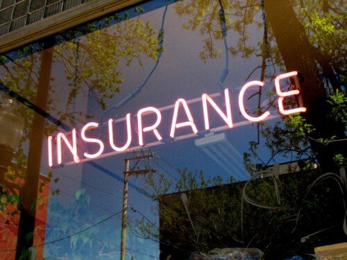 A store front that has a glass window with the word Insurance written on it.